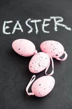Closeup of four pink spotty Easter eggs and text written in chalk on dark background