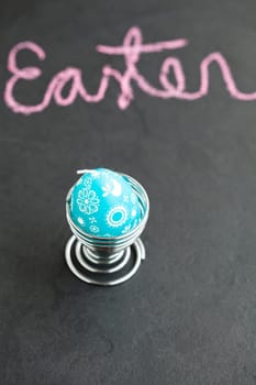 Closeup of blue Easter egg shaped candle with text written in pink chalk