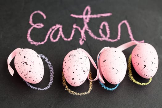 Closeup of four pink spotty Easter eggs and text written in chalk on dark surface