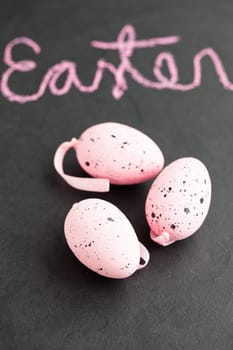 Closeup of three pink spotty Easter eggs and text written in chalk on dark surface