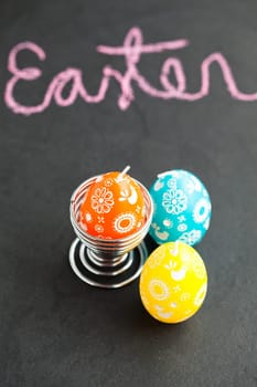 Closeup of three colorful Easter egg shaped candles with text written in pink chalk