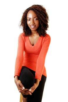 A very tall young teenage girl sitting on a chair in a orange sweater and black tights, smiling, for white background.
