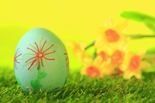 Easter egg painted with floral motif on artificial grass with blurred daffodils in the background
