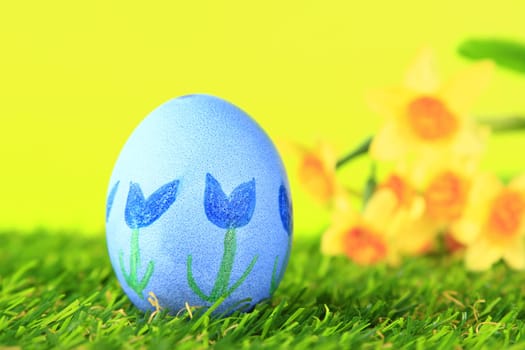 Easter egg painted with floral motif on artificial grass with blurred daffodils in the background