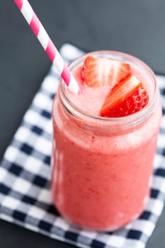 Closeup of fruit smoothie with strawberry slice in glass with straw on checkered napkin