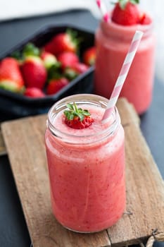Closeup of strawberry fruit smoothies and tray of fresh strawberries in background