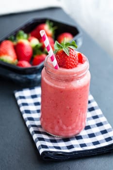 Closeup of strawberry fruit smoothie and tray of fresh strawberries in background