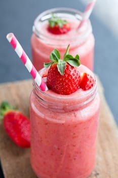 Closeup of strawberry fruit smoothies with strawberry pieces in glass with straw