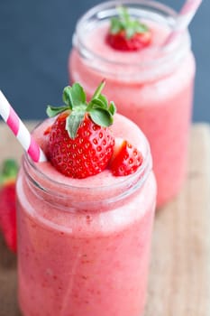 Closeup of strawberry fruit smoothies with strawberry pieces in glass with straw
