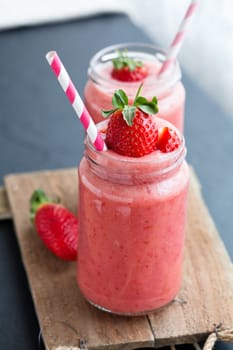 Closeup of strawberry fruit smoothies with strawberry pieces in glass with straw