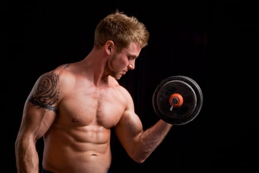Studio photo of young man lifting weights against black background.