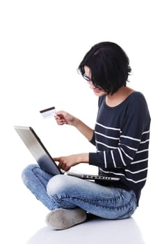 Woman with a laptop and a credit card, sitting on the floor, isolated on white. Buying from internet shoop