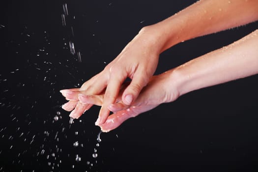 Water falling on female hands, over black background