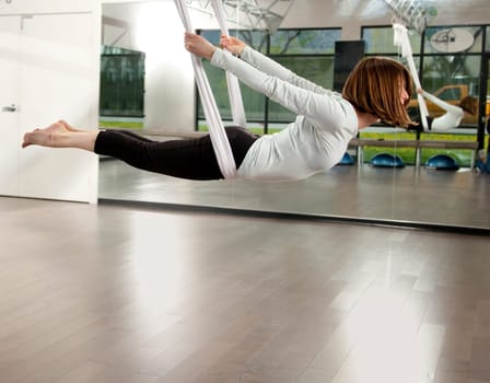 Woman doing anti gravity yoga exercise in fitness center.