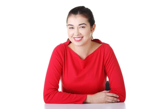 Pretty, happy, young woman in casual clothes sitting at the desk, isolated on white
