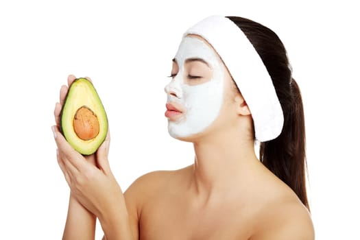 Attractive woman with face clay mask holding avocado. Isolated on white