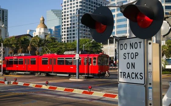 Downtown Scene at RailRoad Crossing Red Trolley Car Passing Signal Lights with Buildings in the Background