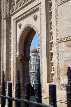Vertical take of the Gateway of India, its black painted railings with a cameo view of the Taj Hotel from an angled view of an archway. Major tourist attraction for visitors to Bombay