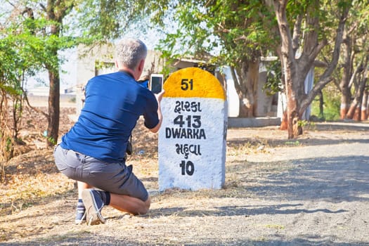 Rural landscape in Gujarat India on the route to Dwarka a holy city for Hindus and Mahabharata, caucasian male taking a photo of the 413 km milestone to Dwarka passing through Mahuva
