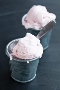 Closeup of strawberry ice cream in two metal cups on dark background