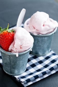 Closeup of strawberry ice cream and strawberry in two metal cups on checkered serviette over dark background