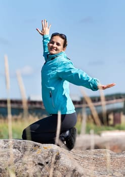 Beautiful girl in a jacket kneeling on a rock, enjoying life and the wind.