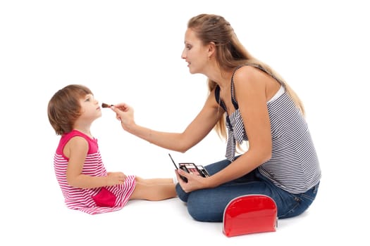 Young mother paints little girl cosmetics on white background