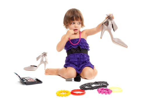 Cute little girl with cosmetics and women's shoes in the studio. Isolate on white.