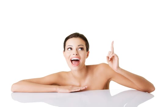 Attractive woman with clean fresh skin pointing on copy space. Isolated on white.