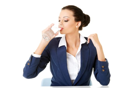 Pretty business woman sitting at the desk and drinking mineral water from glass