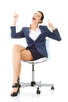 Attractive happy businesswoman sitting on office chair and showing copy space. Isolated on white.