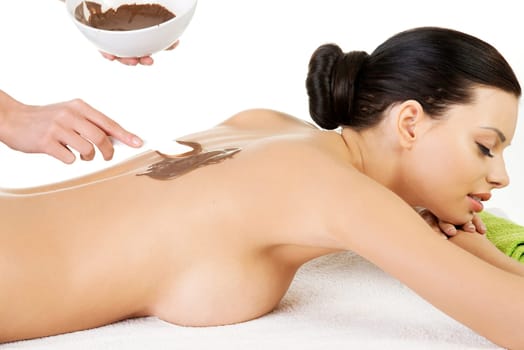 Pretty young woman relaxing being massaged in spa saloon with chocolate. Isoalted on white