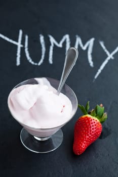 Strawberry ice cream in glass bowl and whole strawberry on dark background with text written in chalk