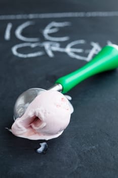 Closeup of strawberry ice cream and scoop on dark background with text written in chalk