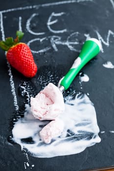 Closeup of strawberry ice cream and scoop and whole straberry on dark background with text written in chalk