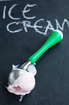 Closeup of strawberry ice cream and scoop on dark background with text written in chalk