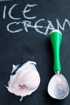 Closeup of strawberry ice cream and scoop on dark background with text written in chalk