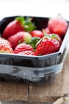 Fresh whole strawberries in plastic packing tray on wooden surface
