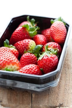 Fresh whole strawberries in plastic packing tray on wooden surface