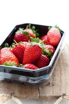 Fresh whole strawberries in plastic packing tray on wooden surface
