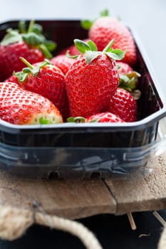 Fresh whole strawberries in plastic packing tray on wooden surface