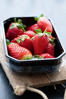 Fresh whole strawberries in plastic packing tray on wooden surface