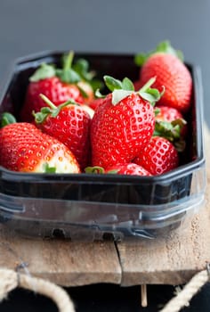 Fresh whole strawberries in plastic packing tray on wooden surface