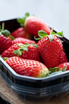 Fresh whole strawberries in plastic packing tray on wooden surface