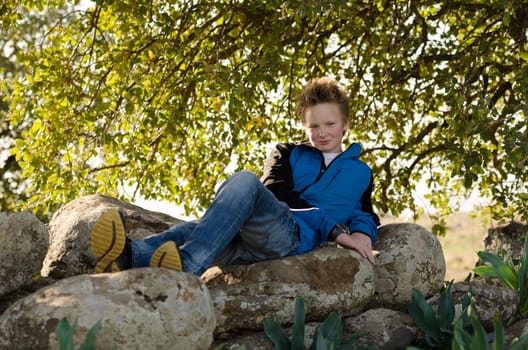 Guy resting in nature on a rock under a tree