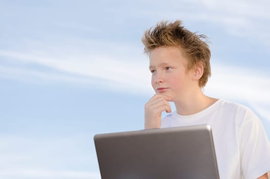 Serious schoolboy with mobile computer think about something on nature