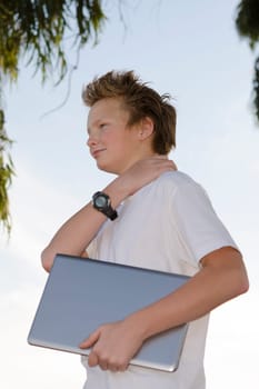 Youngster with notebook stands in nature under tree in profile