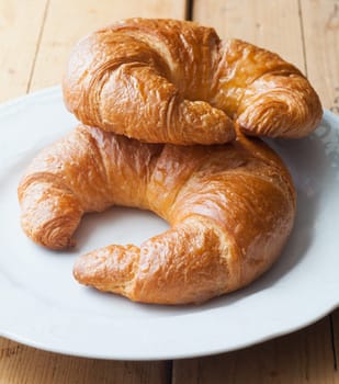 Continental breakfast of two fresh croissants, resting on a white plate on wooden table
