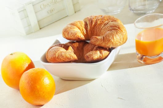 Healthy meal of fresh oranges and crisp golden croissants for breakfast served with a glass of freshly squeezed orange juic