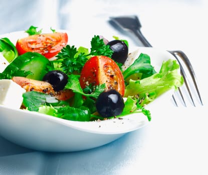 Crisp fresh Greek salad with feta , olives , leafy greens and tomato garnished with parsley